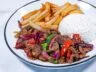 A plated serving of Lomo Saltado with beef, stir-fried vegetables, French fries, and a side of white rice.