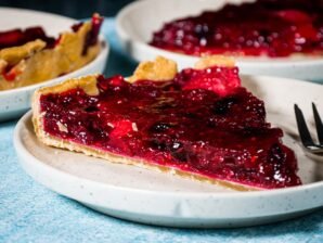 A slice of homemade Mixed Berry Pie with a golden shortcrust pastry and a glossy, vibrant berry filling, served on a white ceramic plate.