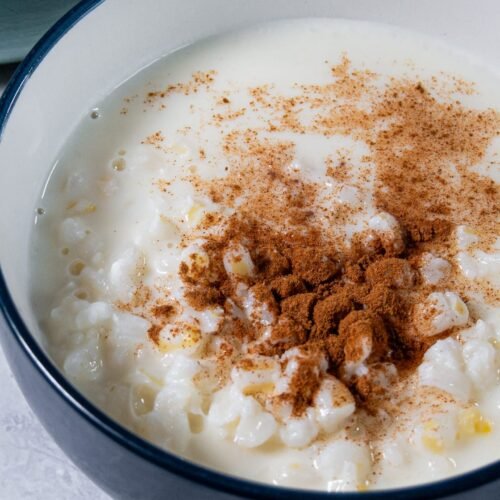 Creamy mungunzá sweet corn porridge topped with cinnamon in a blue bowl.
