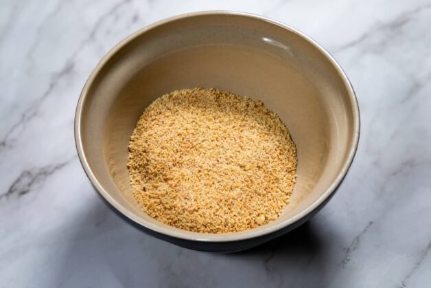 Finely crushed biscuit mix in a beige bowl on a marble countertop.