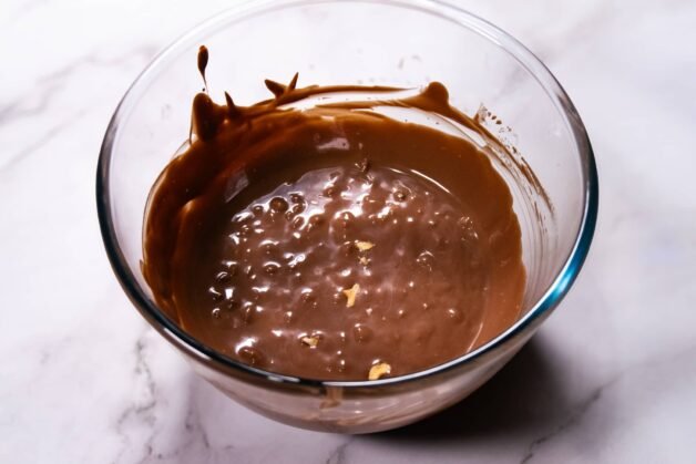 Smooth, melted chocolate coating with chopped hazelnuts in a glass bowl.