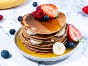 Oatmeal pancakes layered with bananas and garnished with fresh berries on a plate.