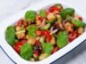 Panzanella salad with roasted bell peppers, crispy bread cubes, fresh basil, and vegetables in a white serving dish.