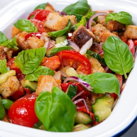 Close-up of Panzanella salad with roasted bell peppers, crunchy bread cubes, fresh basil, and colorful vegetables in a white dish.