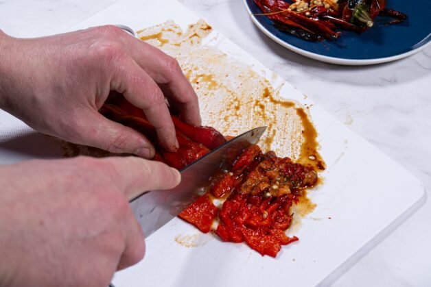 Hands slicing roasted bell peppers on a cutting board for Panzanella salad.
