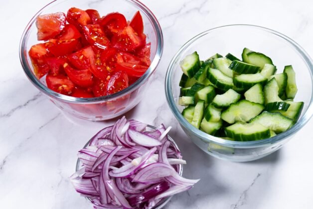 Bowls of diced tomatoes, sliced cucumbers, and red onions prepared for Panzanella salad.