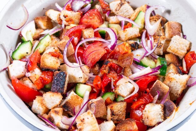 Mixed Panzanella salad with toasted bread, roasted peppers, tomatoes, cucumbers, and red onions in a bowl.