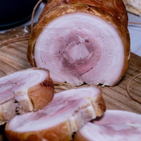 Pork belly roll with slices, served alongside Russian salad and crusty bread.