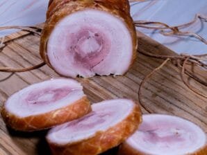 Sliced pork belly roll showing tender meat and crispy crackling on a wooden cutting board.