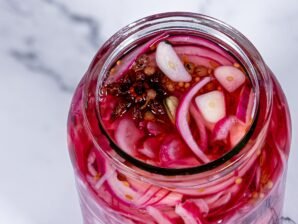 Open jar of pickled red onions showing vibrant pink onion slices, garlic, and spices.