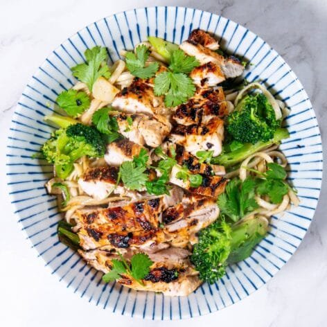 A vibrant bowl of stir-fried Shandon noodles, broccoli, and grilled chicken topped with fresh cilantro.