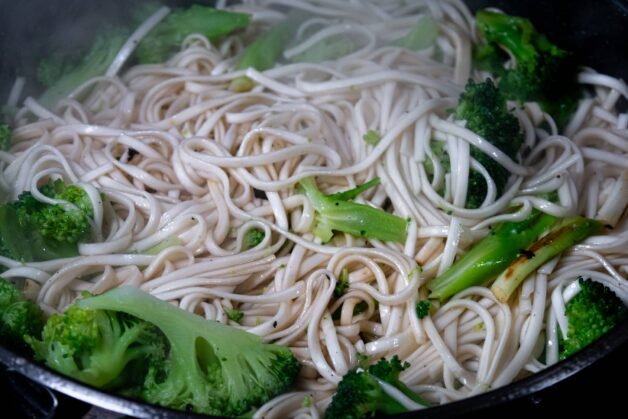 Stir-fried Shandon noodles, broccoli, and scallions in a skillet.