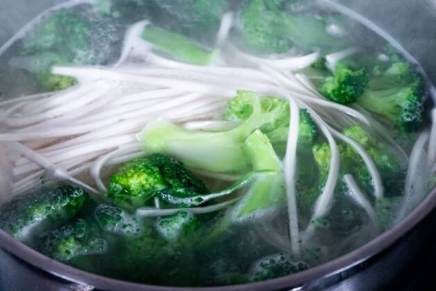 Fresh broccoli and Shandon noodles boiling together in a pot of salted water.