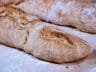 Freshly baked rustic baguettes with a crispy golden crust resting on a parchment-lined baking sheet.