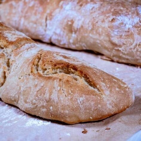 Freshly baked rustic baguettes with a crispy golden crust resting on a parchment-lined baking sheet.