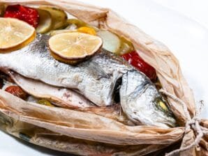 Cooked Sea Bass en Papillote with lemon slices and vegetables peeking through parchment paper.