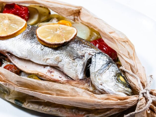 Cooked Sea Bass en Papillote with lemon slices and vegetables peeking through parchment paper.