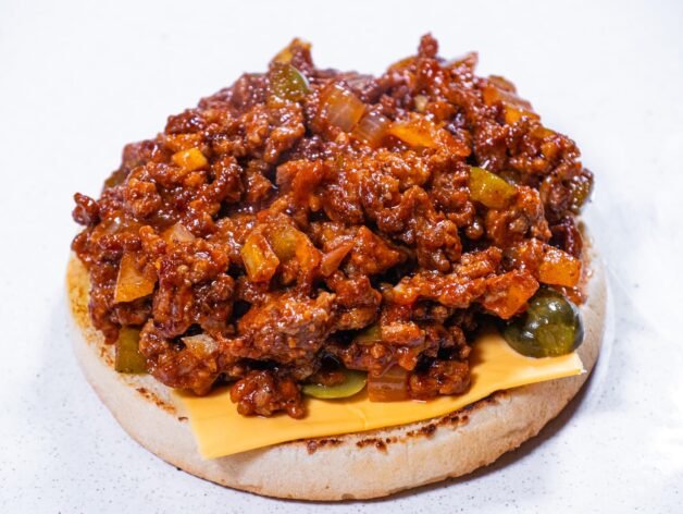 An open-faced Sloppy Joe with cheese, pickles, and saucy beef on a toasted bun.