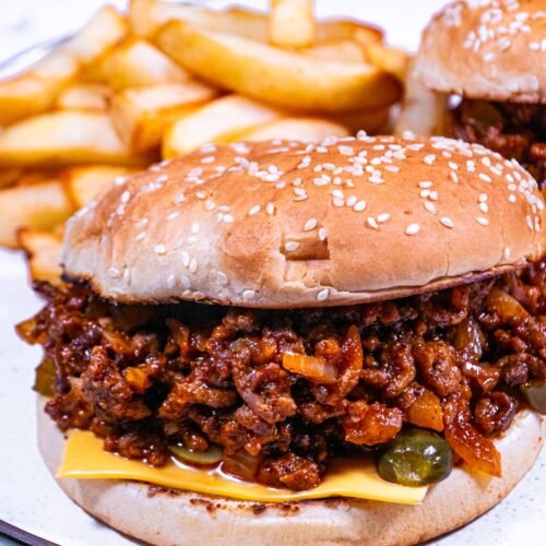 Close-up of homemade Sloppy Joes with melted cheese, pickles, and sesame seed buns.