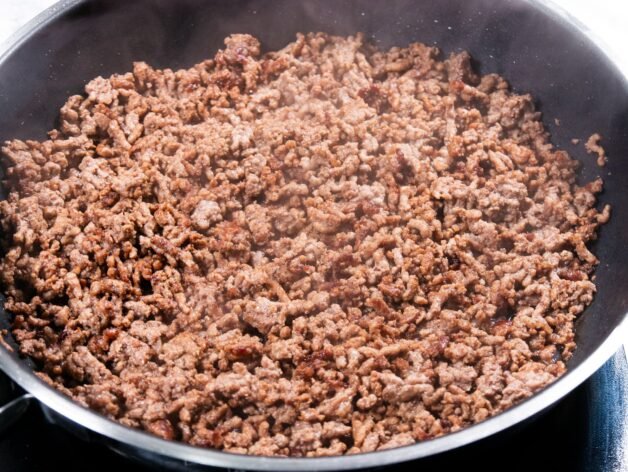 Ground beef browning in a skillet, releasing steam as it cooks.