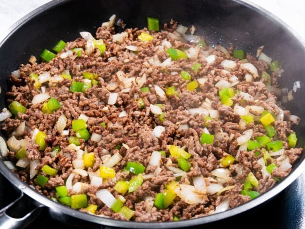 Ground beef mixed with chopped onion, green bell pepper, and garlic in a skillet.