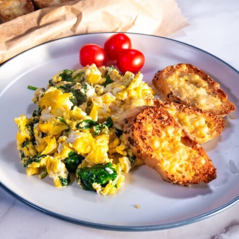 Plate of spinach scrambled eggs served with garlic bread slices and cherry tomatoes.