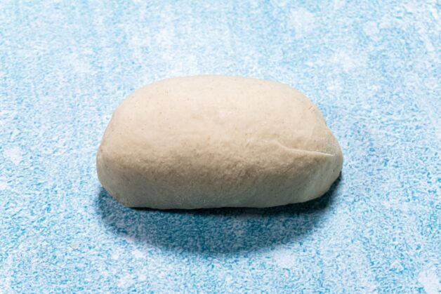A single shaped bun with neatly folded edges, resting on a blue surface.