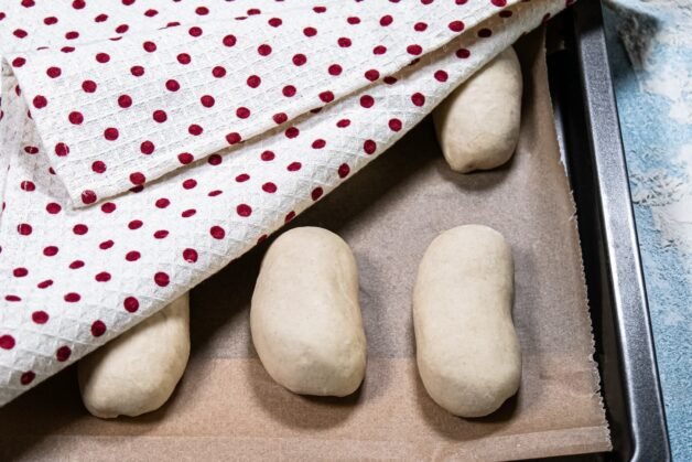 Shaped buns resting on a baking tray, partially covered with a towel.