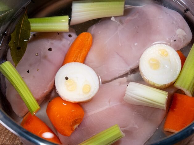 Chicken breasts, celery, carrots, onion, and spices simmering in water to create a flavorful broth.