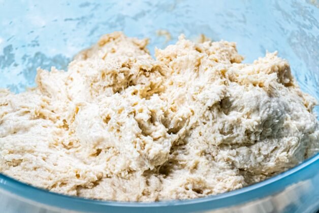 A bowl with dry ingredients and Greek yogurt, with milk being incorporated.