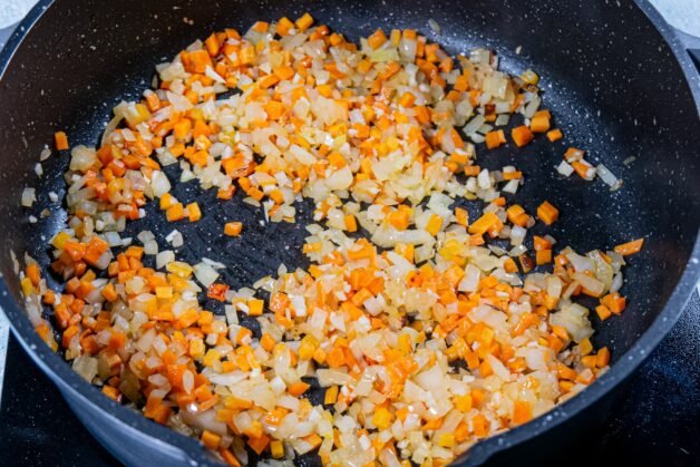 Diced onions, carrots, and garlic sautéing in a pan until softened.