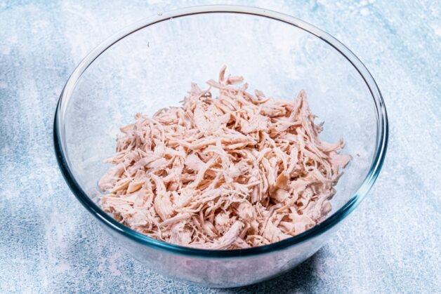 Shredded chicken in a glass bowl, ready to be used in the pie filling.