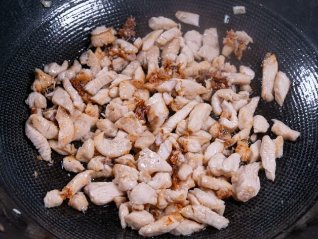 Cooked chicken strips browning in a hot wok.