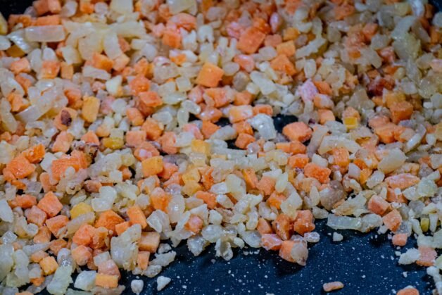 Flour sprinkled over sautéed vegetables in a pan to create a thick filling base.
