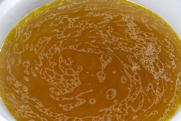 Golden chicken broth in a bowl after straining out vegetables and spices.