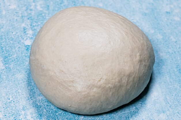 A smooth, well-kneaded ball of dough on a floured surface.