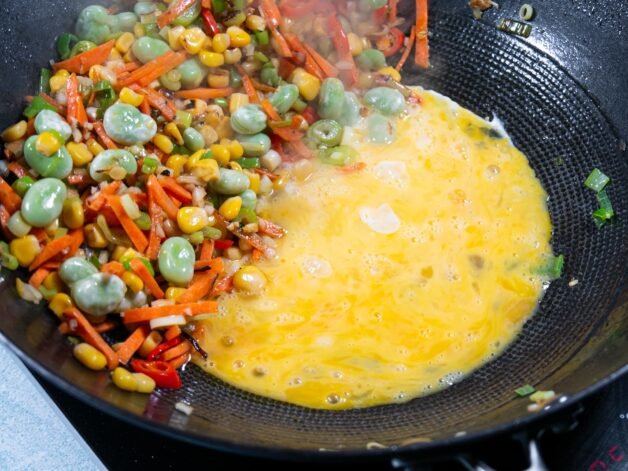 Beaten eggs cooking in the center of a wok with vegetables on the side.