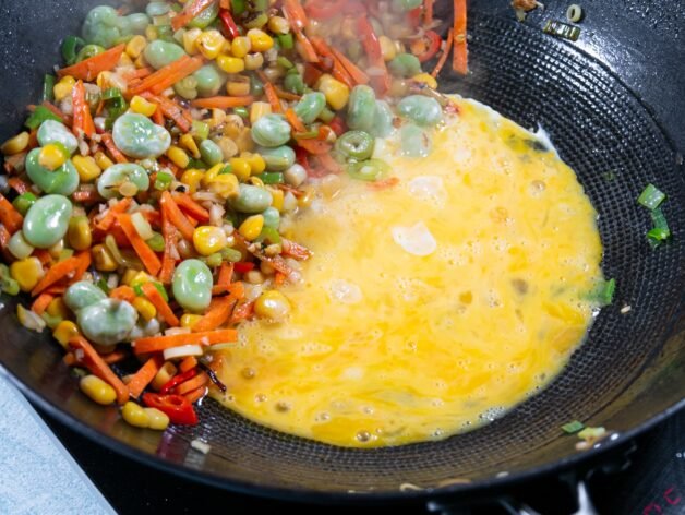Beaten eggs cooking in the center of a wok with vegetables on the side.