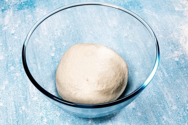 A round dough ball sitting in a glass bowl, ready for proofing.