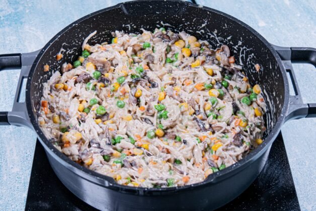 Creamy chicken and mushroom pie filling with peas, corn, and shredded chicken in a pan.