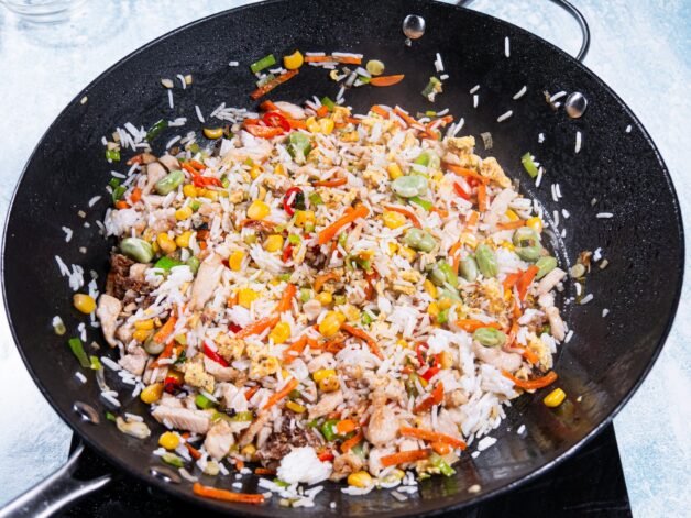Cooked rice and stir-fried ingredients mixed together in a wok.