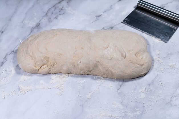 Flatbread dough shaped into a log on a floured surface, ready for dividing.
