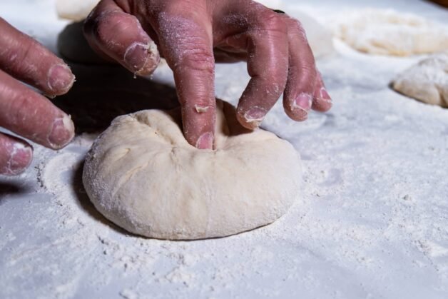 Hands shaping flatbread dough into a ball on a floured surface.