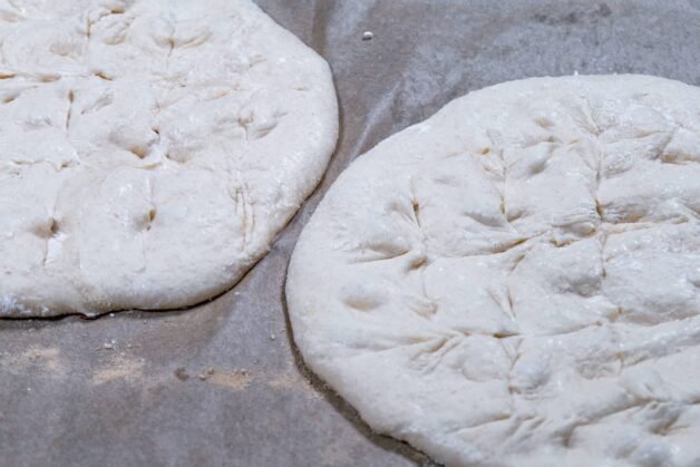 Flatbread dough flattened and scored on parchment paper.