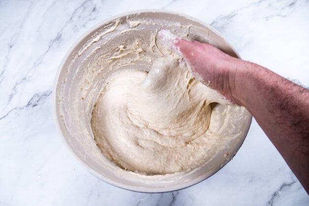 Sticky flatbread dough being stretched by hand in a mixing bowl.