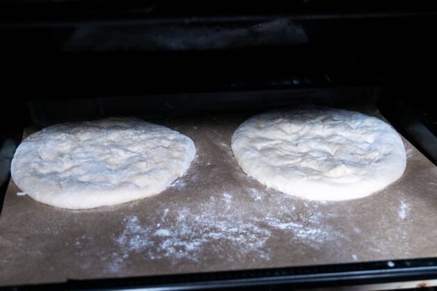Flatbreads baking on parchment paper in an oven.