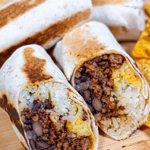 Close-up of a beef burrito cut in half, showing seasoned beef, rice, black beans, and melted cheese wrapped in a crispy tortilla.