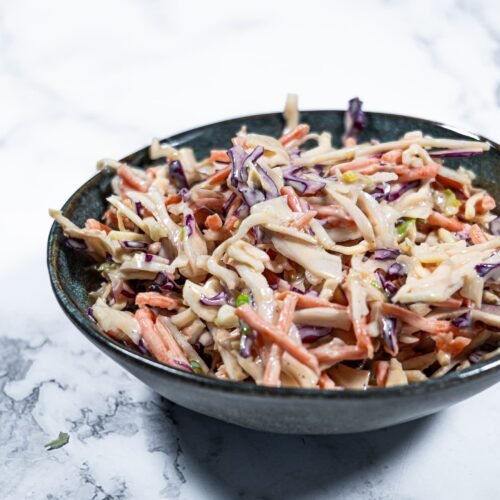 Creamy coleslaw salad with shredded cabbage, carrots, and a tangy dressing, served in a dark bowl.