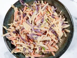 Top-down view of creamy coleslaw salad with shredded green and red cabbage, carrots, and a tangy dressing in a dark bowl.