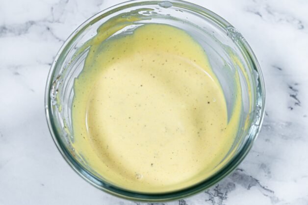 A glass bowl filled with creamy coleslaw dressing made with mayonnaise, Greek yogurt, Dijon mustard, and apple cider vinegar.